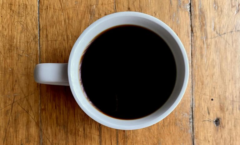 A simple white mug filled with black coffee on a rustic wooden table.